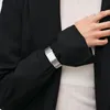 A close-up shot of a person's wrist wearing a silver watch and a black blazer. Produktbild-Vorschau