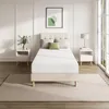 A bedroom scene with a mattress on a bed frame, bedside tables, and a rug. Produktbild-Vorschau