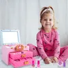 A young girl is sitting on a bed next to a pink makeup case. Produktbild-Vorschau