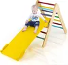 A baby is sitting on a yellow slide attached to a wooden climbing triangle.