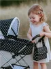 A young girl is playing with a doll stroller outdoors. Anteprima dell’immagine prodotto