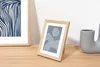Two framed pictures and a vase are displayed on a wooden surface against a white wall. Produktbild-Vorschau