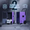 Two purple dehumidifiers are shown in a studio-like setting with a concrete floor and wall. One dehumidifier is open, showing a water tank, and the other has a hose connected for continuous drainage. Anteprima dell’immagine prodotto