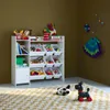 A child's toy storage unit filled with toys, placed in a room with a brown wall and a patterned rug. Produktbild-Vorschau