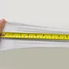 A hand is stretching a white fabric with a measuring tape to show its elasticity. Produktbild-Vorschau