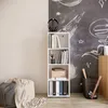 A white bookshelf with books and binders is placed next to a wall with chalk drawings. Produktbild-Vorschau