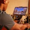 A person is using an exercise bike with a tablet mounted on it, displaying a virtual cycling game. Produktbild-Vorschau