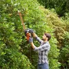 A man is trimming a hedge with an electric hedge trimmer. Produktbild-Vorschau