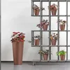 A tall, copper-colored planter with a red-leafed plant stands to the left of a gray metal shelving unit displaying several smaller potted plants. Náhľad obrázku produktu
