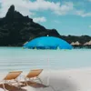 A beach scene with a blue umbrella and two lounge chairs in the foreground, and overwater bungalows and a mountain in the background. Voir les images du produit