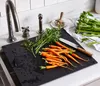 Carrots and celery are being prepared for cooking on a black cutting board next to a kitchen sink and faucet. Náhled obrázku produktu