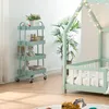 A mint green kitchen roll cart with four shelves is shown next to a bed frame decorated with fairy lights and a potted plant. Anteprima dell’immagine prodotto