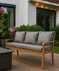 A wooden bench with gray cushions sits on a wooden deck, surrounded by plants and a house. Voir les images du produit