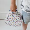 A child's hand holding a round, patterned case. Produktbild-Vorschau