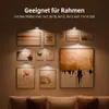 Silberne Bildleuchten, die verschiedene gerahmte Kunstwerke an einer braunen Wand über einem Sofa beleuchten Náhled obrázku produktu