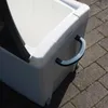 A close-up view of a white cooler box with a gray handle, resting on a paved surface. Produktbild-Vorschau