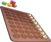 A silicone baking mat with circular indentations for making macarons, with a few macarons shown at the top left and some filling being piped onto the mat. Podgląd zdjęcia produktu