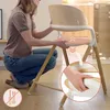 A person is demonstrating how to adjust a part of a wooden high chair. Voir les images du produit