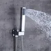 A modern chrome shower head mounted on a textured gray wall, with water spraying out. Produktbild-Vorschau