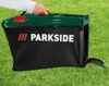 A hand is holding a grass catcher bag for a lawnmower, which is placed on a green lawn. Produktbild-Vorschau