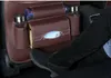 A person's legs and feet are visible in the foreground, with a brown car seat organizer attached to the back of a car seat. The organizer has multiple pockets holding items like bottles and tissues. Podgląd zdjęcia produktu
