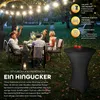 A group of people are enjoying a meal outdoors at a table, with string lights overhead. Produktbild-Vorschau