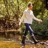 A woman walking through a shallow stream in a wooded area. Produktbild-Vorschau