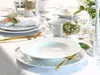 A beautifully set dining table with white porcelain plates, gold cutlery, and small floral arrangements. Produktbild-Vorschau