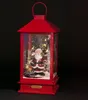 A red lantern with a Santa Claus figurine inside, illuminated by LED lights and surrounded by artificial snow and miniature Christmas trees. Produktbild-Vorschau