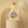 A bottle of Woolite laundry detergent is displayed on a pedestal against a backdrop of curved, layered shapes and draped fabric. Podgląd zdjęcia produktu
