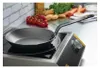 A de Buyer Mineral B frying pan sits on an induction cooktop, with vegetables in the background. Náhľad obrázku produktu