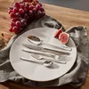 A set of cutlery is arranged on a plate, with grapes and figs nearby, on a wooden table. Anteprima dell’immagine prodotto