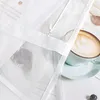 A close-up view of a white sheer curtain with a coffee cup and saucer in the background. Produktbild-Vorschau