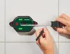 A person is using a PARKSIDE® Digitale Laserwasserwaage with a roll-out tape measure to mark a line on a tiled wall. Produktbild-Vorschau