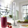 A white immersion blender and a glass of berry smoothie on a kitchen counter with some fruit and a bowl of soup. Voir les images du produit