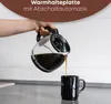 A hand pouring coffee from a glass carafe into a black mug. Náhľad obrázku produktu