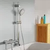 A showerhead and hose assembly mounted on a rail, with a bathtub edge visible in the foreground and a wooden cabinet with bottles in the background. Náhled obrázku produktu