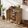 A wooden shoe cabinet filled with shoes, placed in a room with a plant and a stool. Náhľad obrázku produktu