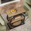 A wooden side table with a metal frame, placed on a rug next to a sofa. The table has two shelves and is decorated with a bowl of fruit and books. Anteprima dell’immagine prodotto