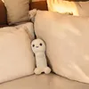 A plush toy is nestled between several large, soft pillows on a bed or sofa. Náhled obrázku produktu