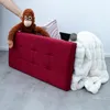 A stuffed orangutan and a stuffed hippo are placed on a red ottoman with a white blanket draped over it. A hand is visible, holding the orangutan. Náhled obrázku produktu