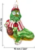 A glass Christmas ornament shaped like a green crocodile wearing a red and white striped shirt and a red cap, holding a brown ball. Náhled obrázku produktu