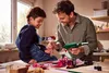 A father and son are crafting together, using a hot glue gun to assemble paper flowers. Produktbild-Vorschau