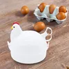 A white chicken-shaped egg cooker is placed on a wooden surface next to a carton of brown eggs. Produktbild-Vorschau