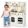 A young child stands in front of a wooden toy kitchen. Produktbild-Vorschau
