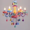 A colorful, whimsical chandelier with multiple candle-shaped lights and hanging decorative elements. Produktbild-Vorschau