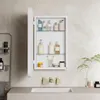 A white medicine cabinet with a mirror door is open, revealing shelves stocked with various toiletries and bathroom products. It is mounted on a tiled wall above a sink. Produktbild-Vorschau