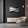 A modern living room scene featuring a framed artwork above a wooden cabinet and a woven chair. Náhled obrázku produktu