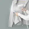 A person is using a handheld garment steamer on a gray hooded sweatshirt hanging on a hanger. Produktbild-Vorschau