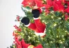 A close-up shot of a Christmas tree decorated with lights, red poinsettias, and a pair of Santa Claus legs sticking out from the branches. Produktbild-Vorschau
